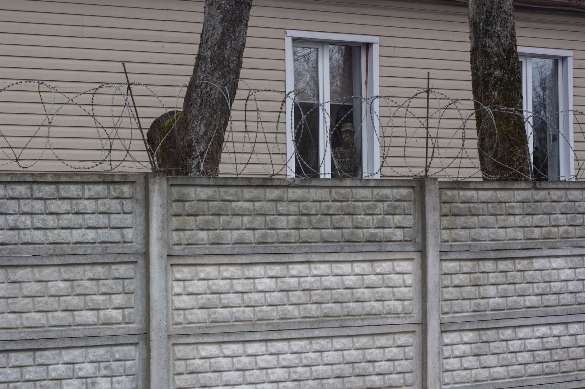 Betonowy mur z drutem kolczastym przed domem z dwoma oknami