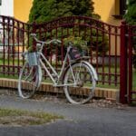Ogrodzenie z gabionów i lameli kompozytowych – jak ciekawie zaaranżować front posesji? Zabytkowy rower z koszem kwiatów przed czerwonym kut